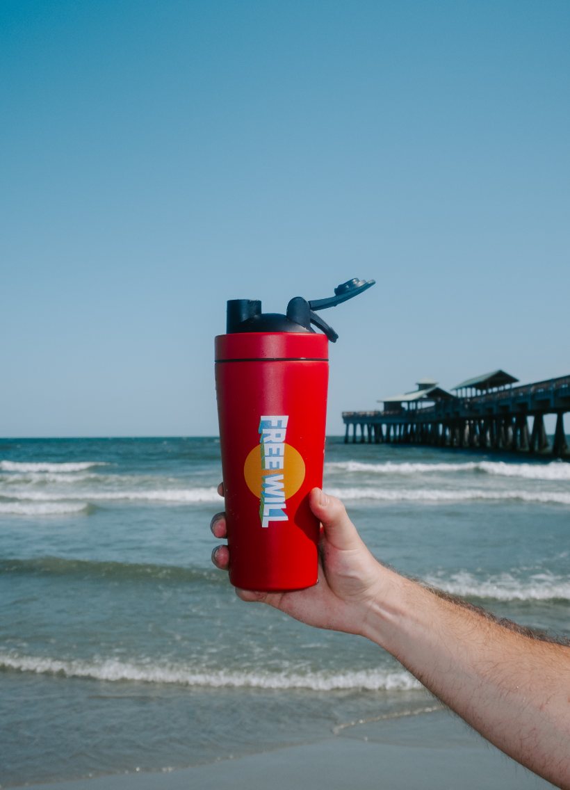 A Free Will shaker held up against the ocean and pier