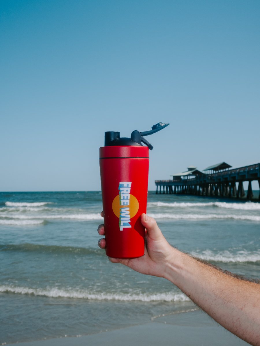 A Free Will shaker held up against the ocean and pier